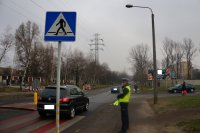 policjant stoi przy oznakowanym przejściu dla pieszych z odblaskami