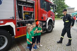 na zdjęciu dzieci w kasku strażaka  stoją przy wozie strażackim ze strażakiem