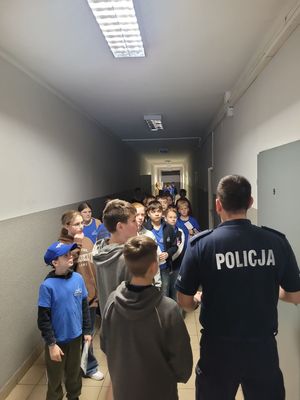 na zdjęciu policjant i uczniowie na korytarzu komendy